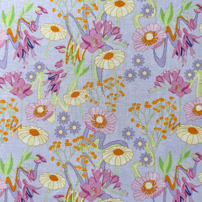 Retro Bloom fabric laid flat, featuring pink blooms, pale yellow daisies, tiny purple flowers and orange details on a pale lilac background.