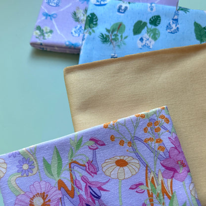 Close-up of retro floral fabric on lilac alongside plain yellow and blue and lilac potted plant fabrics, showing their texture.
