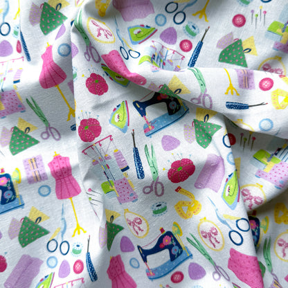 Draped sewing print fabric showing its texture and sewing-room motifs in pink, lilac, green, yellow and blue.