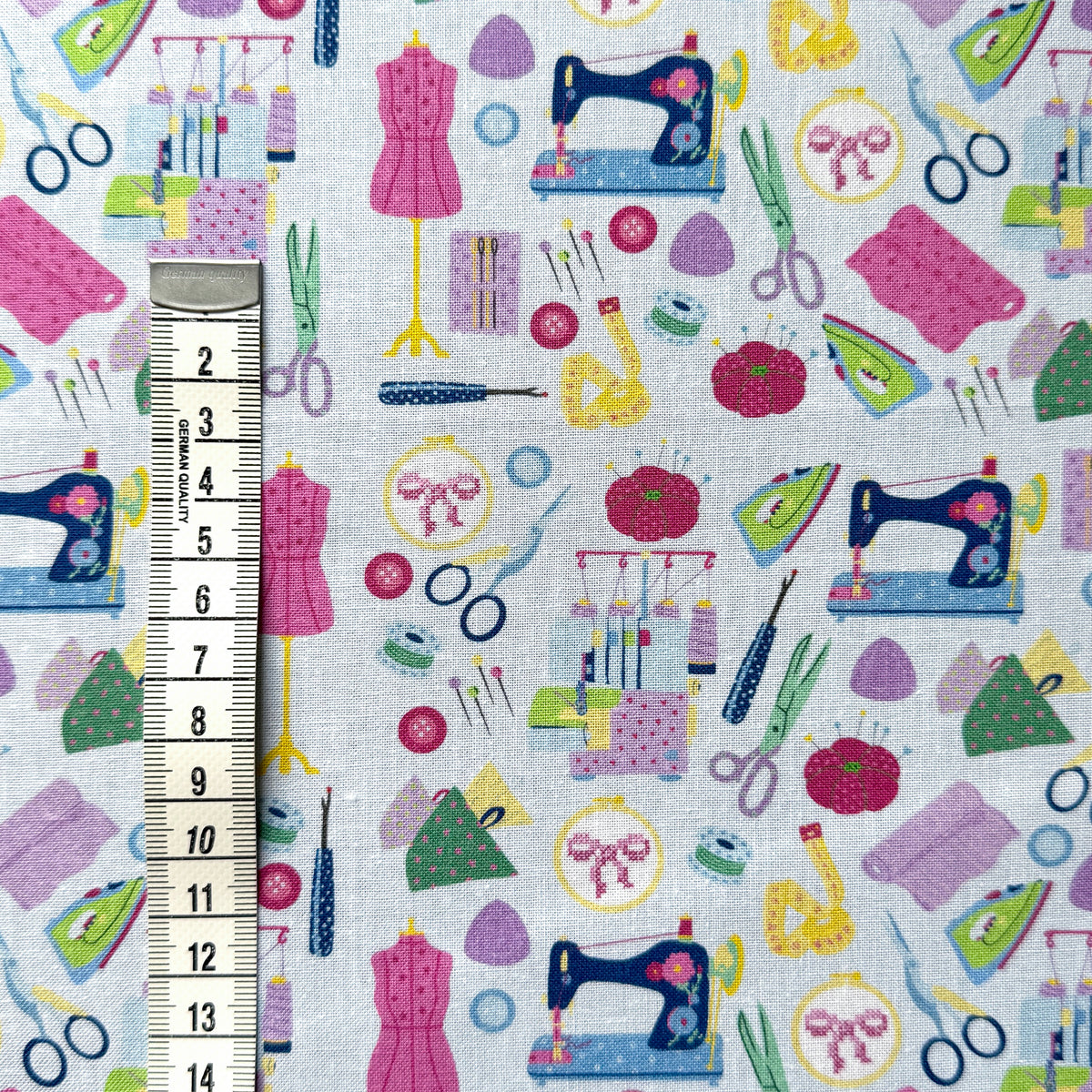 Sewing-themed fabric beside a centimetre tape measure to show the scale of the sewing machines, scissors and dress forms.
