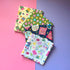 Four folded sewing-themed fat quarters fanned out, featuring thread spools, colourful thimbles, embroidery hoops and sewing tools. The hand designed sewing fabric features overlockers, scissors, fabric weights, tape measure, pin cushion, sewing machine, iron, bobbins and more. 