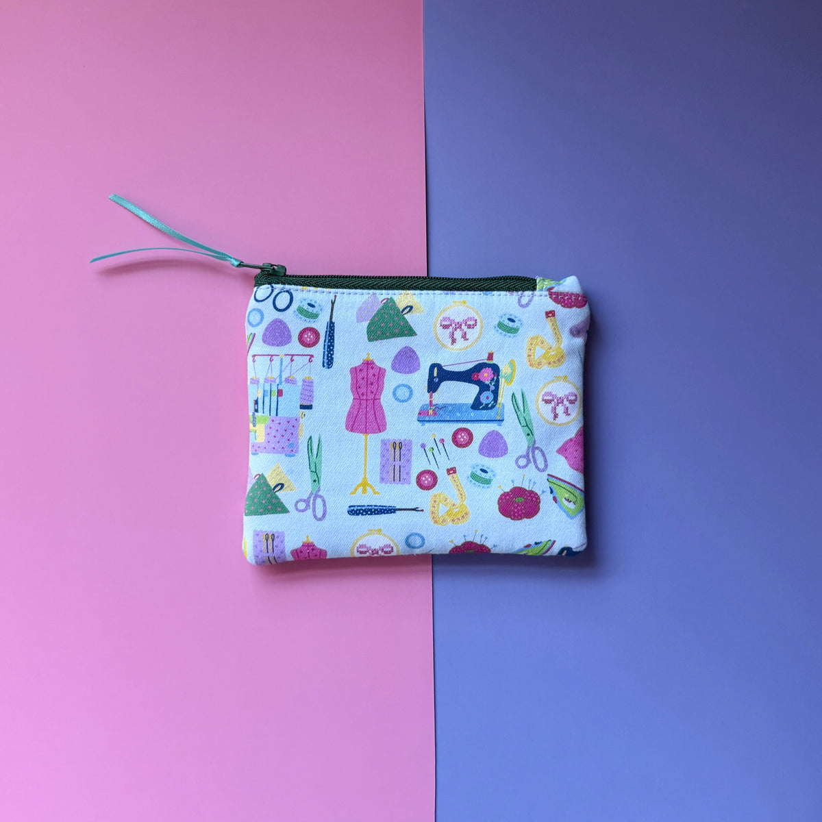Back of the small sewing pouch, showing colourful sewing motifs on pale blue fabric and a green zip.