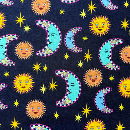 Navy celestial fabric laid flat, featuring golden sun faces, turquoise and blue crescent moons with pink outlines, and yellow stars.
