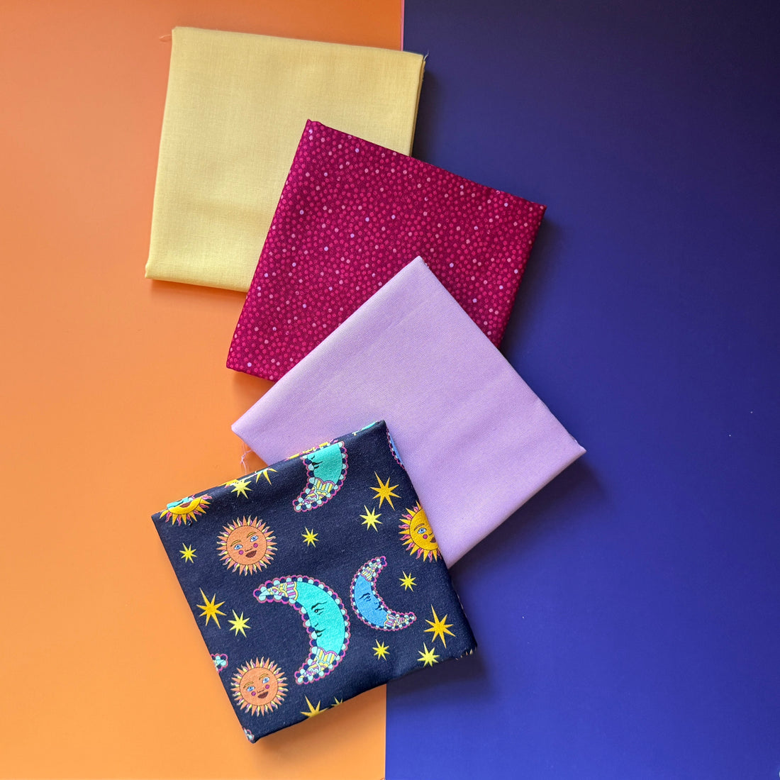 Four folded fat quarters overlapping diagonally, with navy sun and moon print in front of lilac, berry pink and pale yellow fabrics.
