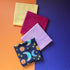 Four folded fat quarters overlapping diagonally, with navy sun and moon print in front of lilac, berry pink and pale yellow fabrics.
