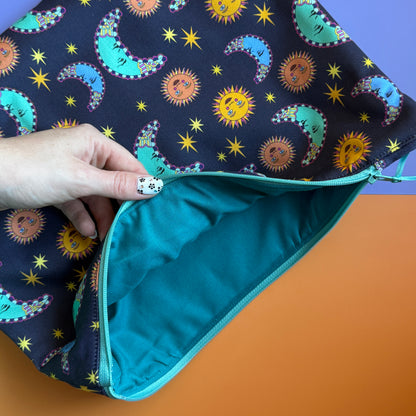 Sun and moon print pouch held open to show its plain dark green fabric lining and turquoise zip.