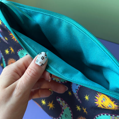 Close-up of a zip wash bag opened by a hand with black-and-white floral nail art, showing a turquoise water repellant interior and a navy celestial exterior. 